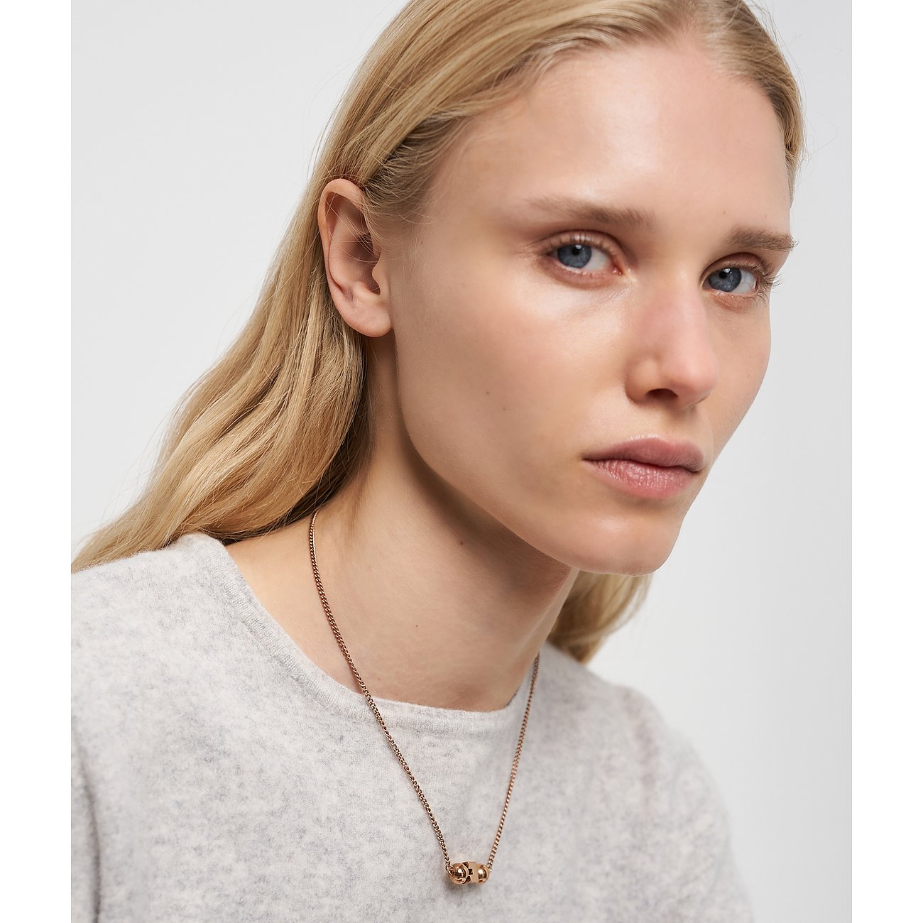 Närbild av kvinna som bär ett roséguldfärgat Liebeskind-halsband i rostfritt stål med två små runda berlocker.