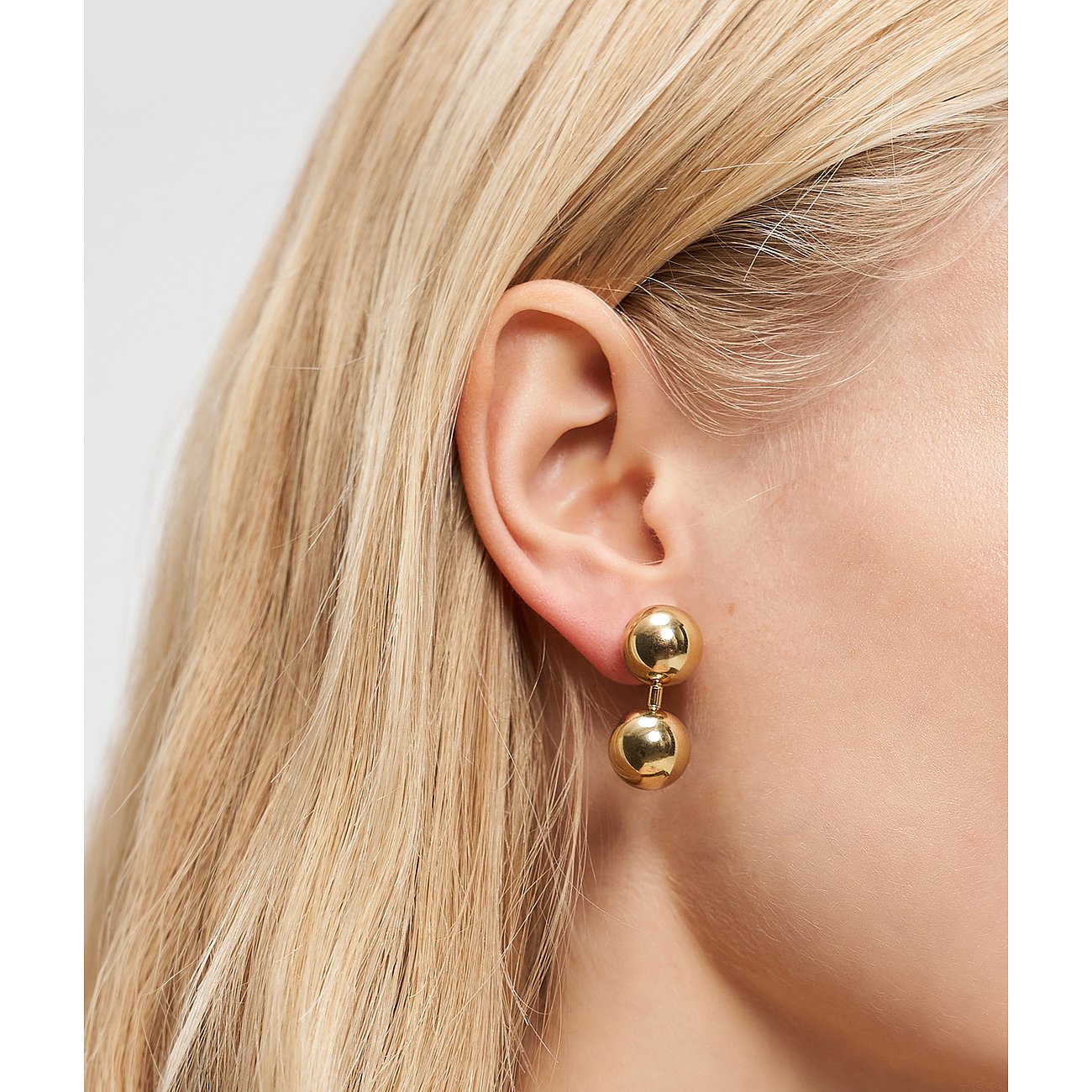 Am Ohr getragenes Liebeskind Ohrschmuck aus gelb vergoldetem Edelstahl mit zwei glänzenden Kugeln.