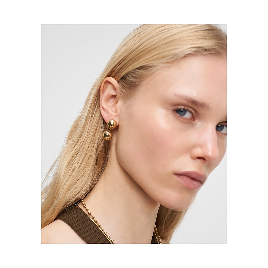 Nahaufnahme einer Frau, die goldfarbene Liebeskind Ohrstecker aus Edelstahl mit zwei Kugeln trägt.