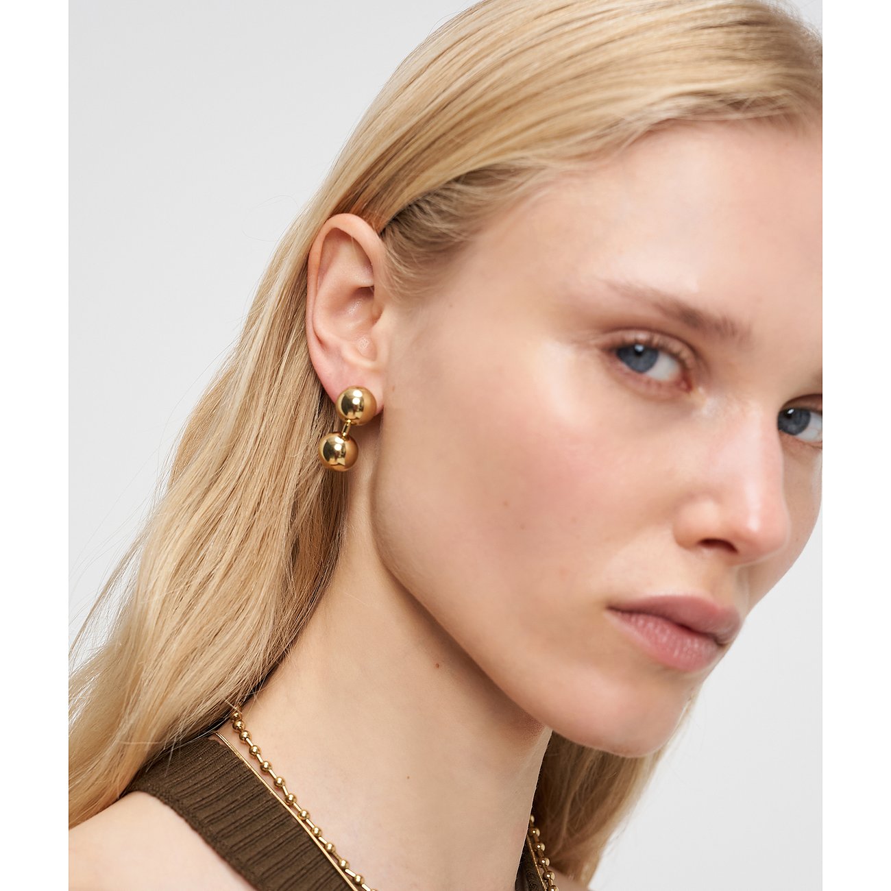 Nahaufnahme einer Frau, die goldfarbene Liebeskind Ohrstecker aus Edelstahl mit zwei Kugeln trägt.