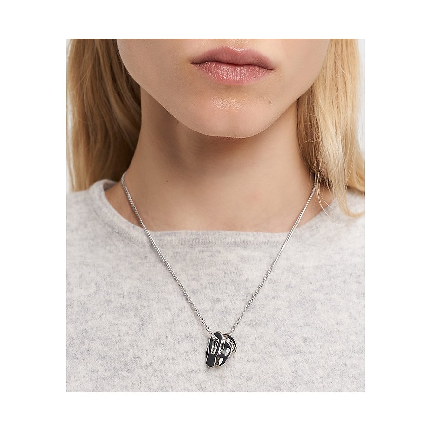 Nahaufnahme einer Frau, die eine Liebeskind Halskette aus Edelstahl mit einem skulpturalen, glänzenden Anhänger trägt.