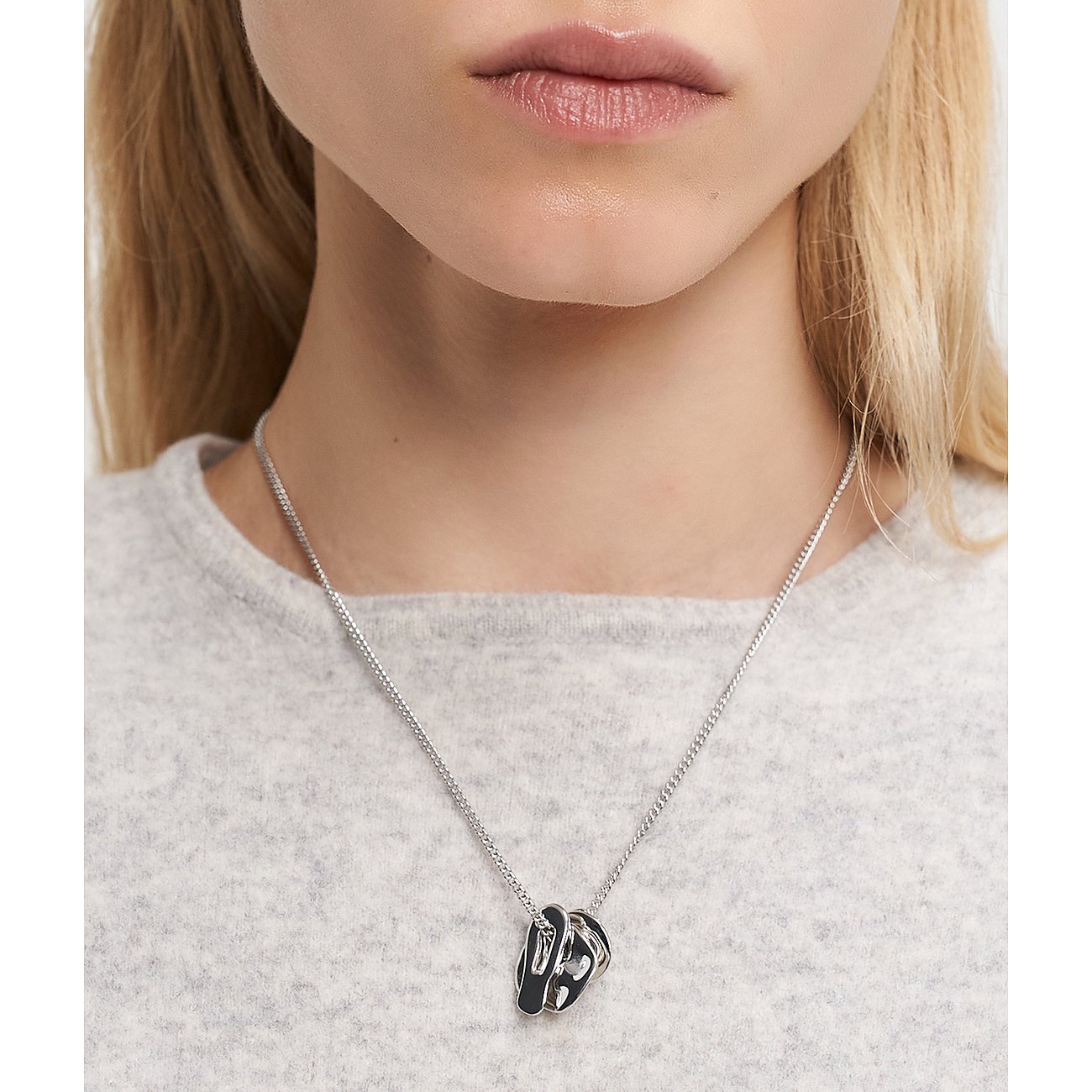 Nahaufnahme einer Frau, die eine Liebeskind Halskette aus Edelstahl mit einem skulpturalen, glänzenden Anhänger trägt.