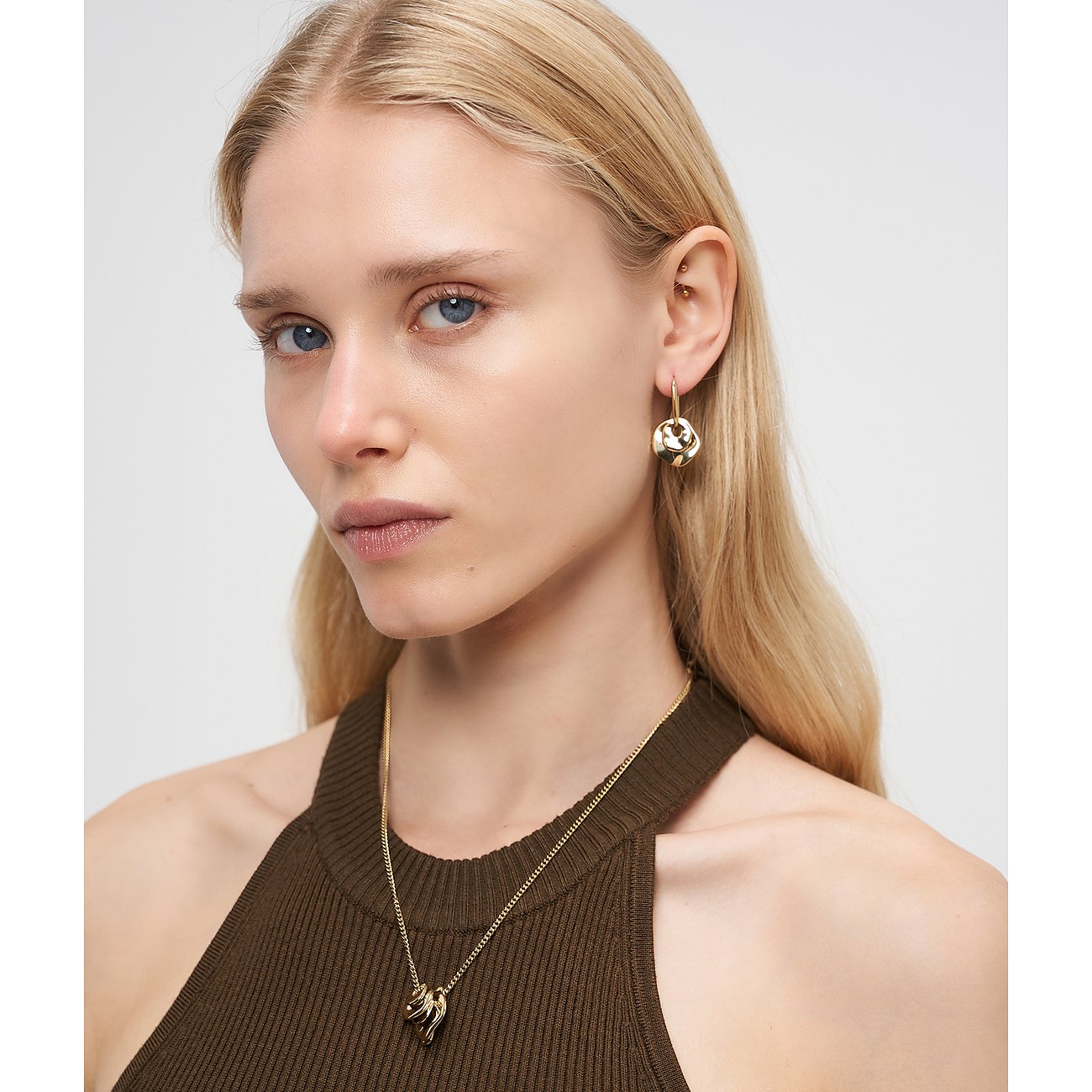 Eine blonde Frau tr g einen eleganten Halsschmuck und Ohrringe der Marke Liebeskind aus goldfarbenem Edelstahl.