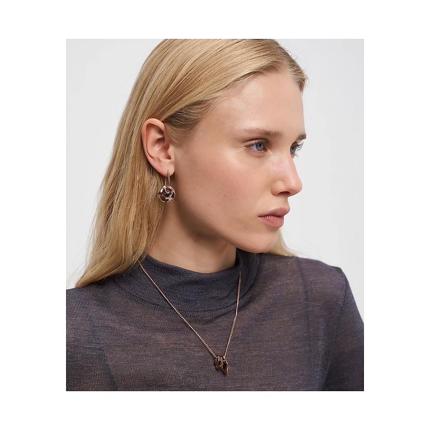 Model trägt Liebeskind Halsschmuck aus goldfarbenem Edelstahl und passende Ohrringe mit Flechtmuster.
