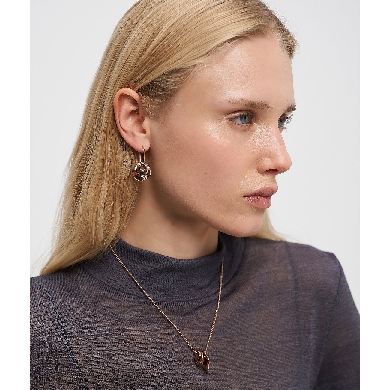 Model trägt Liebeskind Halsschmuck aus goldfarbenem Edelstahl und passende Ohrringe mit Flechtmuster.