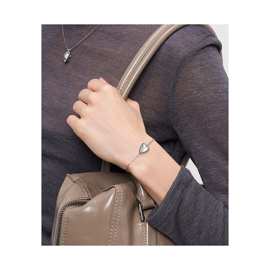 Närbild: Liebeskind armband i rostfritt stål med hjärtberlock på handleden hos person med beige läderväska.