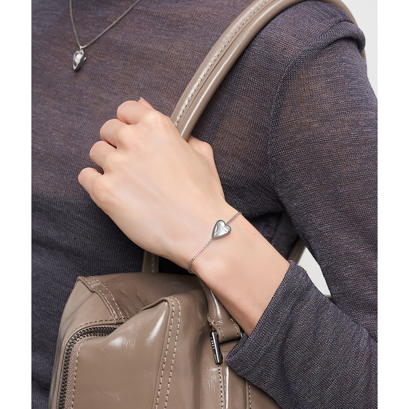 Närbild: Liebeskind armband i rostfritt stål med hjärtberlock på handleden hos person med beige läderväska.