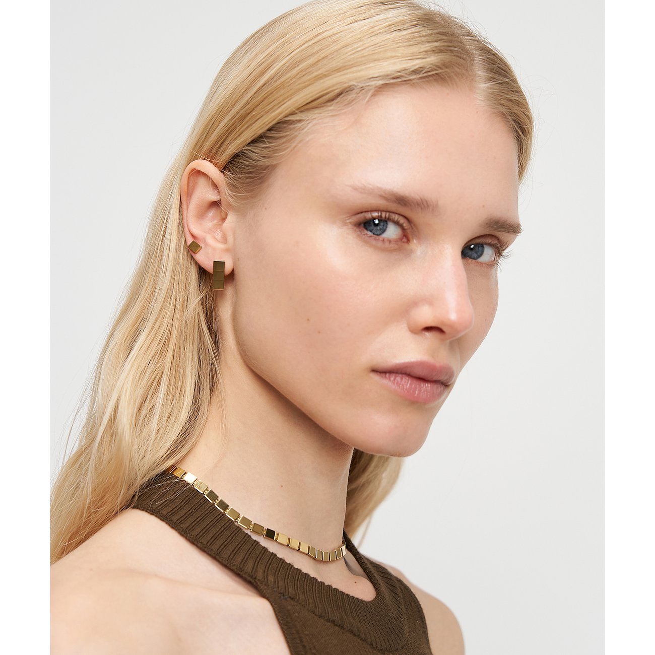 Nahaufnahme einer Frau, die goldfarbenen Liebeskind Edelstahlohrschmuck in geometrischen Formen trägt.