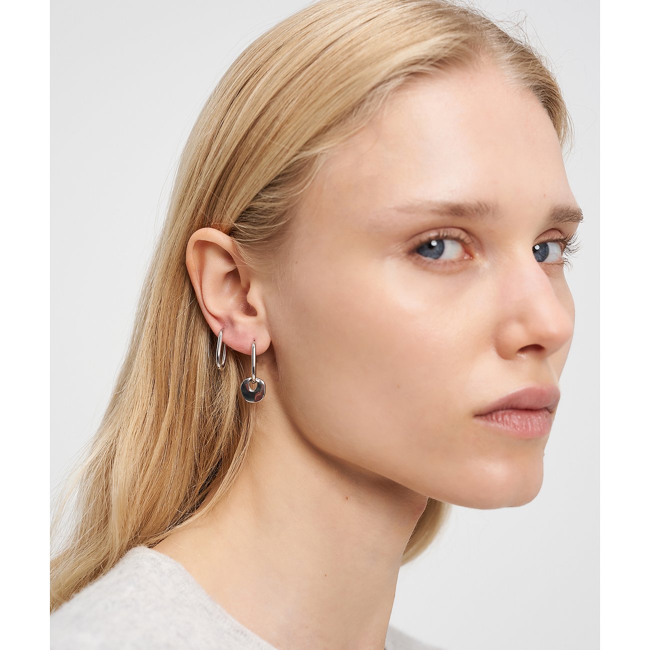 Blonde Frau von der Seite mit Liebeskind Edelstahl-Ohrringen: baumelnde Scheiben und kleine kreisförmige Creole.