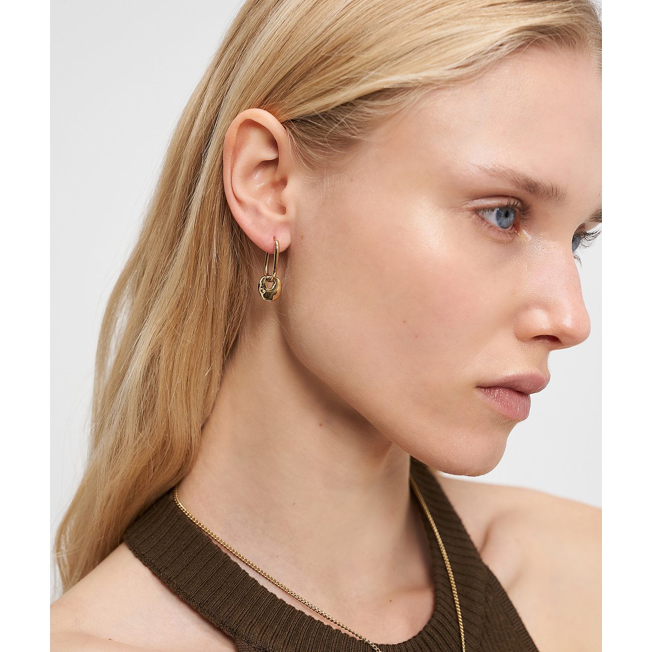 Een vrouw draagt een gouden Liebeskind roestvrijstalen oorbel met een hangende, gestructureerde hanger aan haar rechteroor.