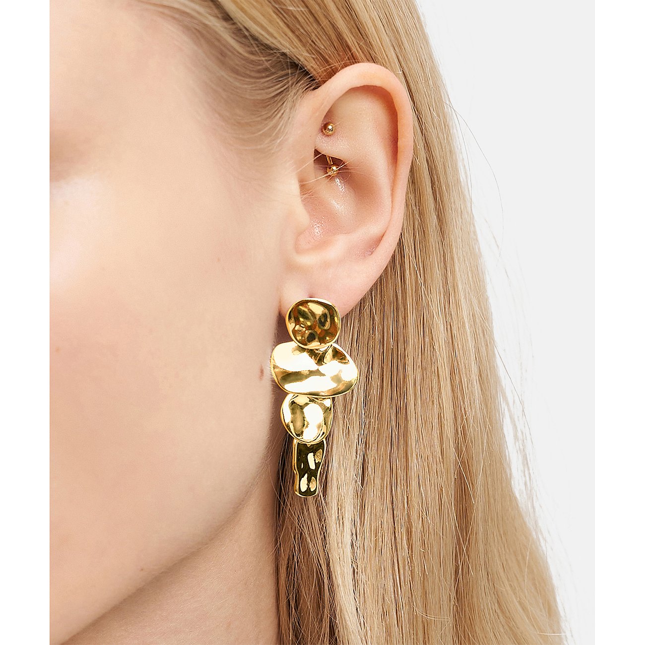 Nahaufnahme: Liebeskind Ohrschmuck aus goldenem Edelstahl mit unregelmäßig gehämmerten Elementen am Ohr eines Models.