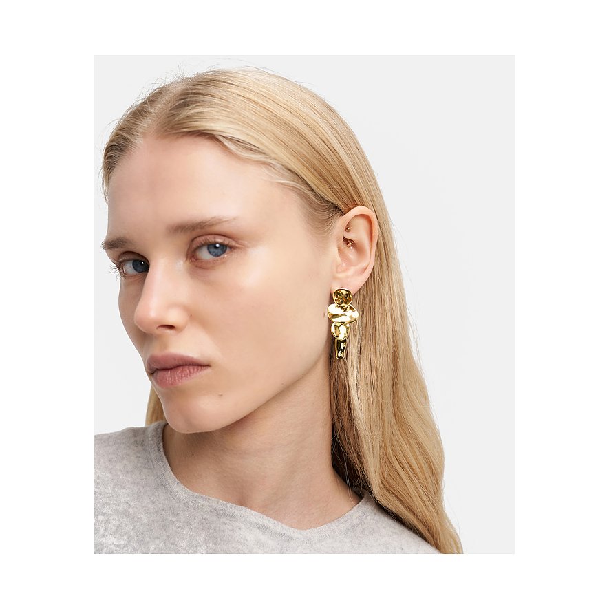 Eine Frau trägt einen goldenen Ohrschmuck von Liebeskind aus Edelstahl, der aus organisch geformten Elementen besteht.