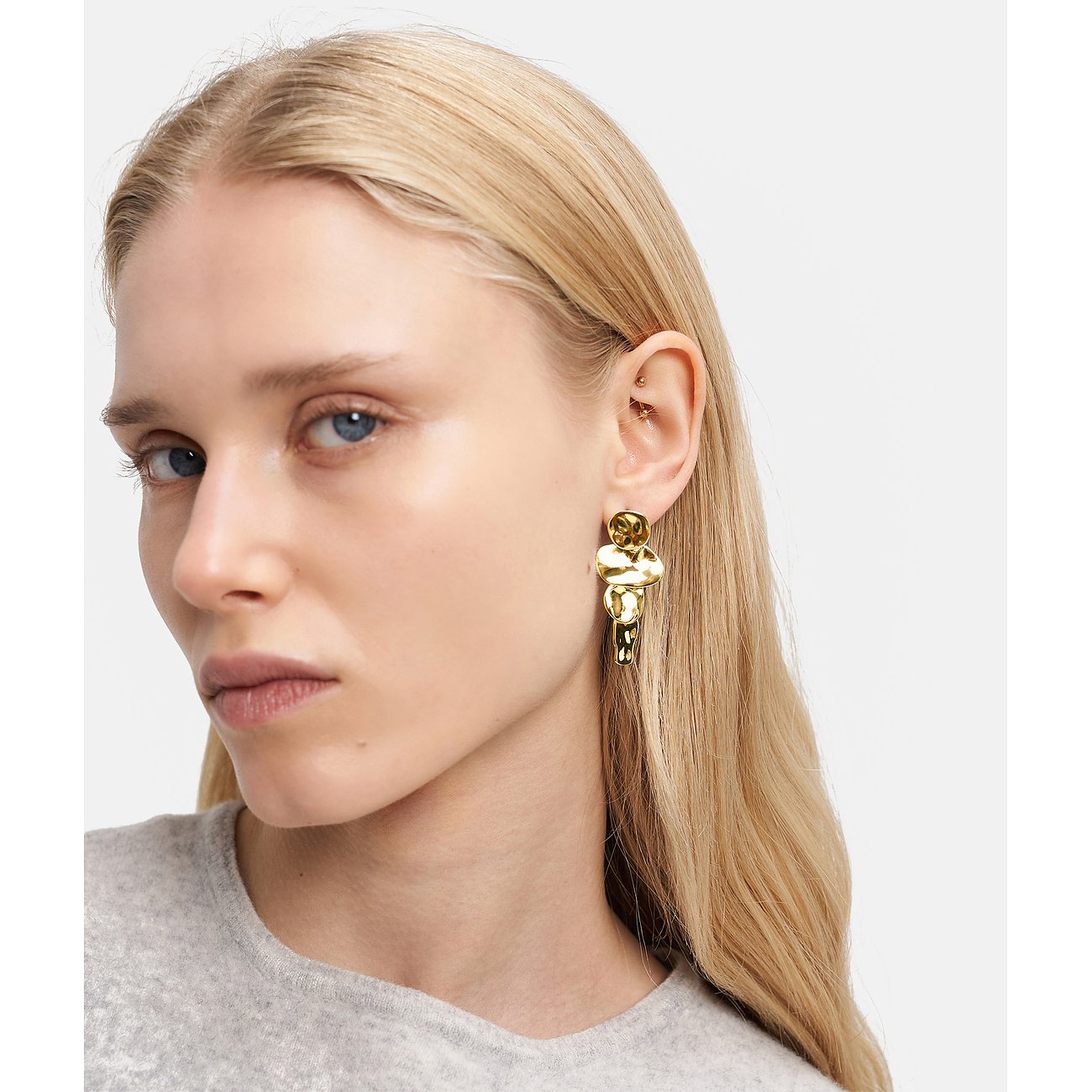 Eine Frau trägt einen goldenen Ohrschmuck von Liebeskind aus Edelstahl, der aus organisch geformten Elementen besteht.