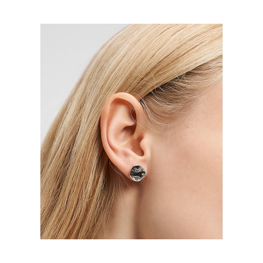 Primo piano di un orecchino a perno Liebeskind in acciaio inox martellato, indossato su un orecchio con capelli biondi.