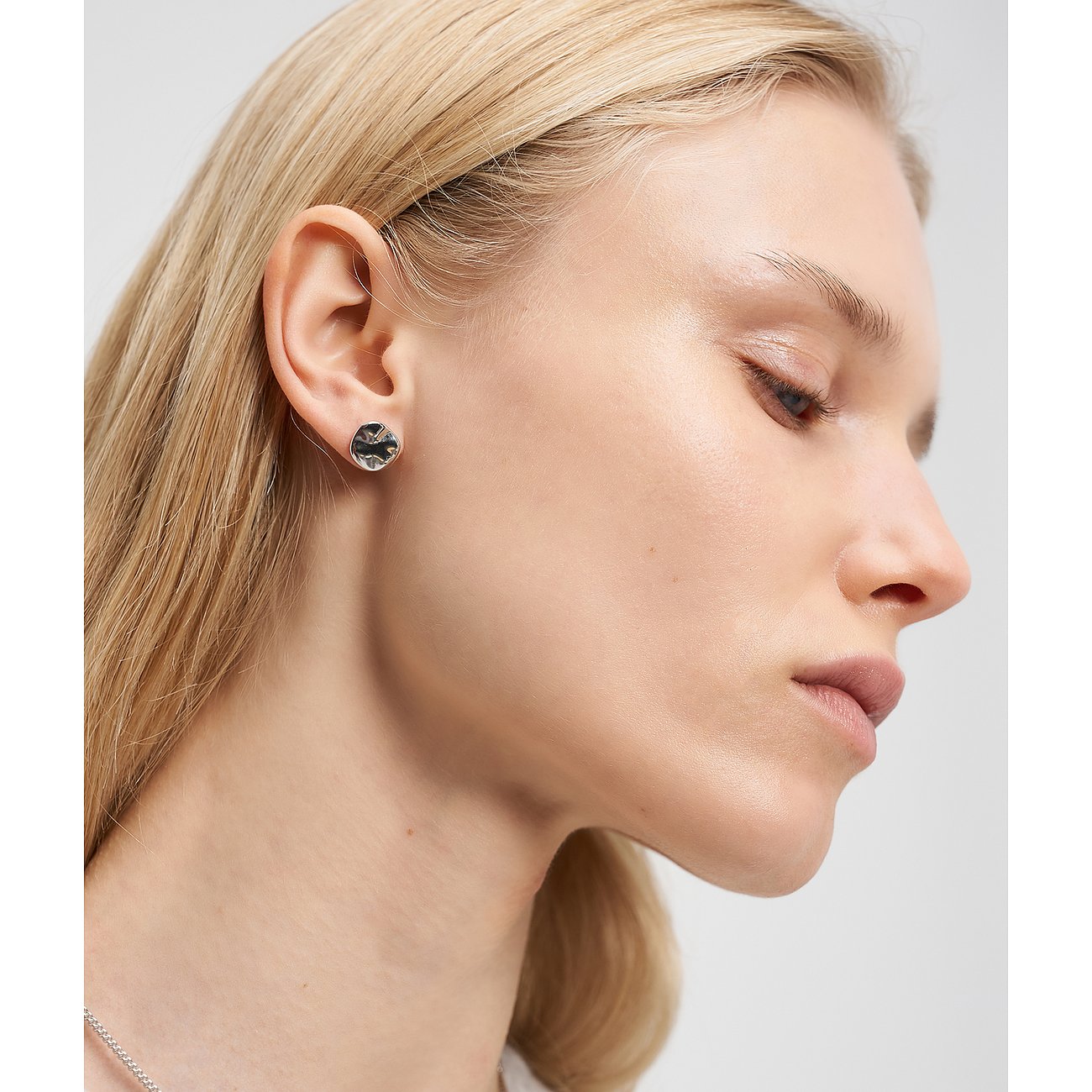 Una donna indossa un orecchino a lobo rotondo Liebeskind in acciaio inox con una gemma chiara tagliata sull'orecchio destro.