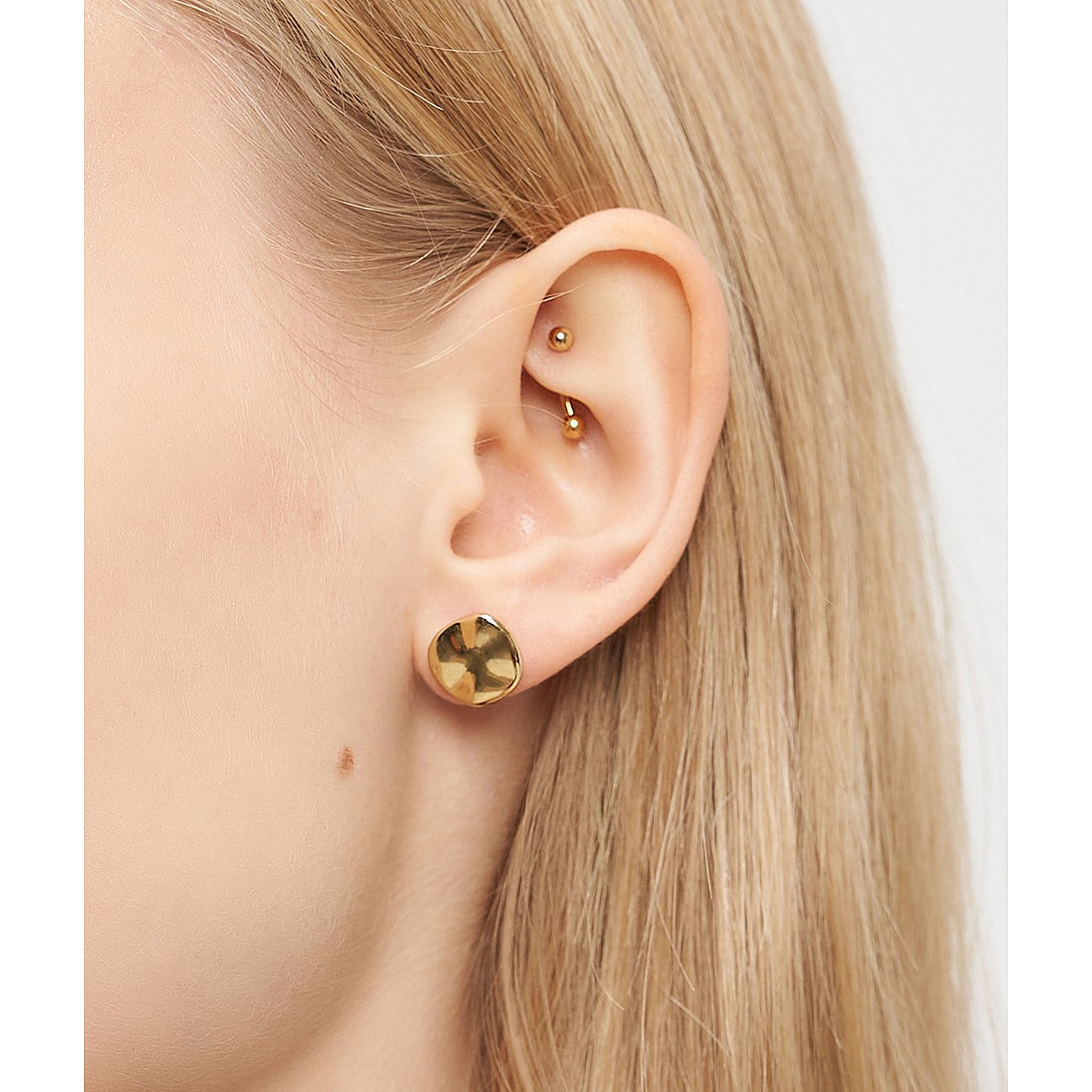 Primo piano di un orecchio con orecchino Liebeskind in acciaio inossidabile placcato oro, forma a disco martellato.