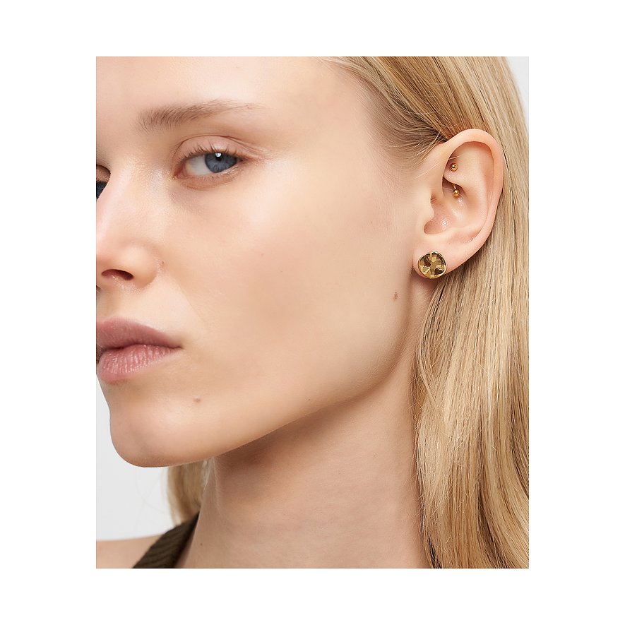 Primo piano di donna con orecchini a perno Liebeskind in acciaio inox, che mostrano pietre scintillanti color miele.