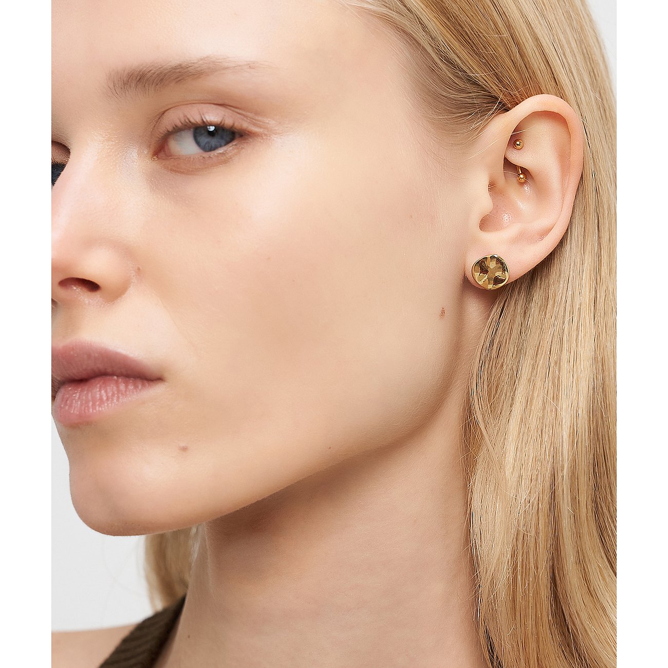 Primo piano di donna con orecchini a perno Liebeskind in acciaio inox, che mostrano pietre scintillanti color miele.