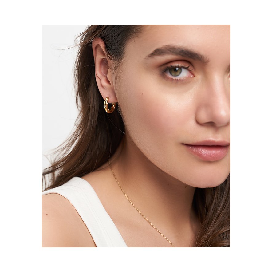 Närbild: Kvinna med allvarlig blick, bär Tamaris örhänge i guldfärgat rostfritt stål, smyckat med gnistrande glasstenar.