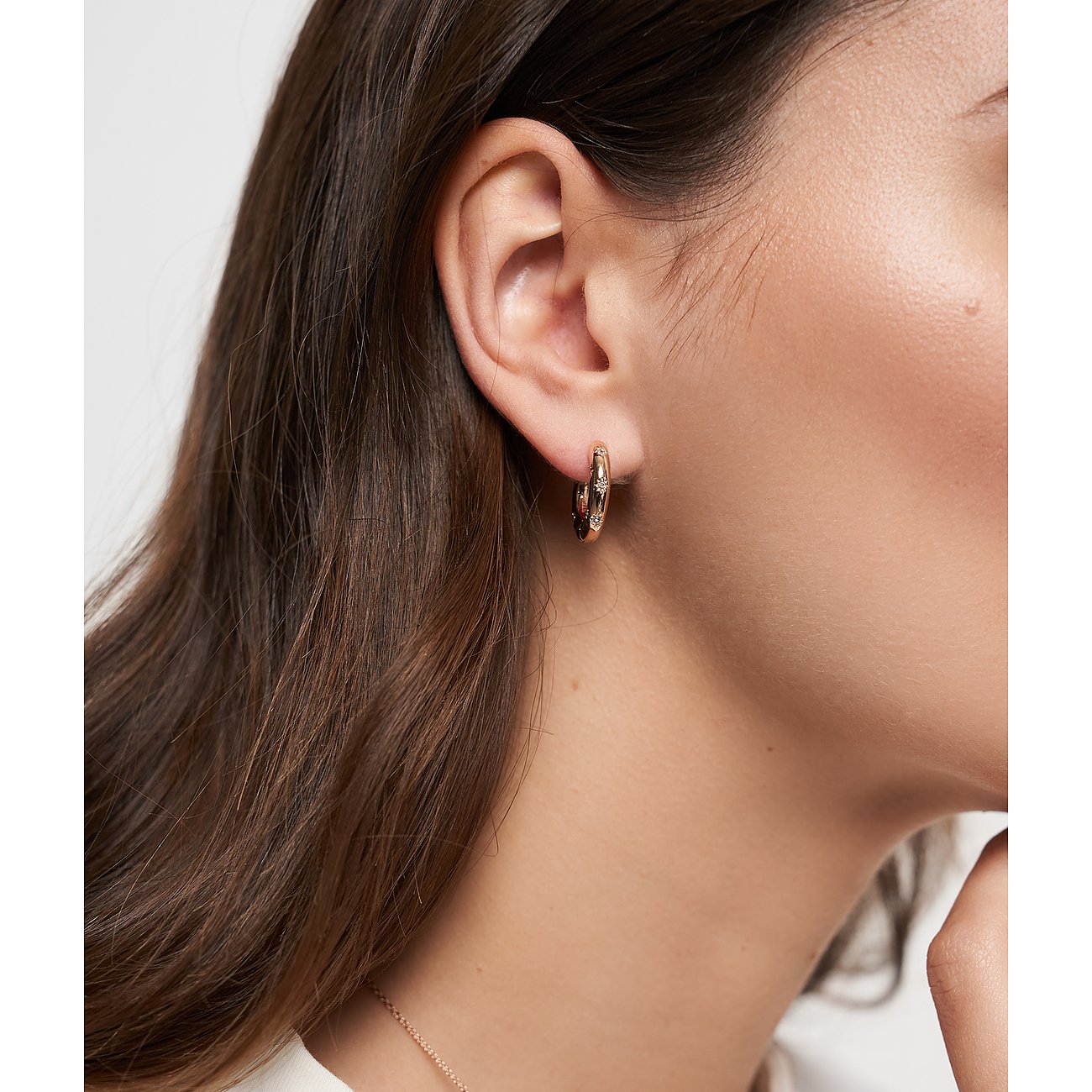 Am Ohr einer Frau ist ein Tamaris Creolen-Ohrring aus roségoldfarbenem Edelstahl mit glänzenden Glassteinen zu sehen.