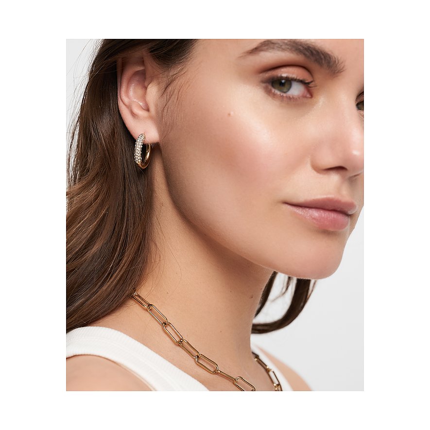 Närbild av kvinna med gyllene Tamaris creoler i rostfritt stål, besatta med gnistrande glasstenar.