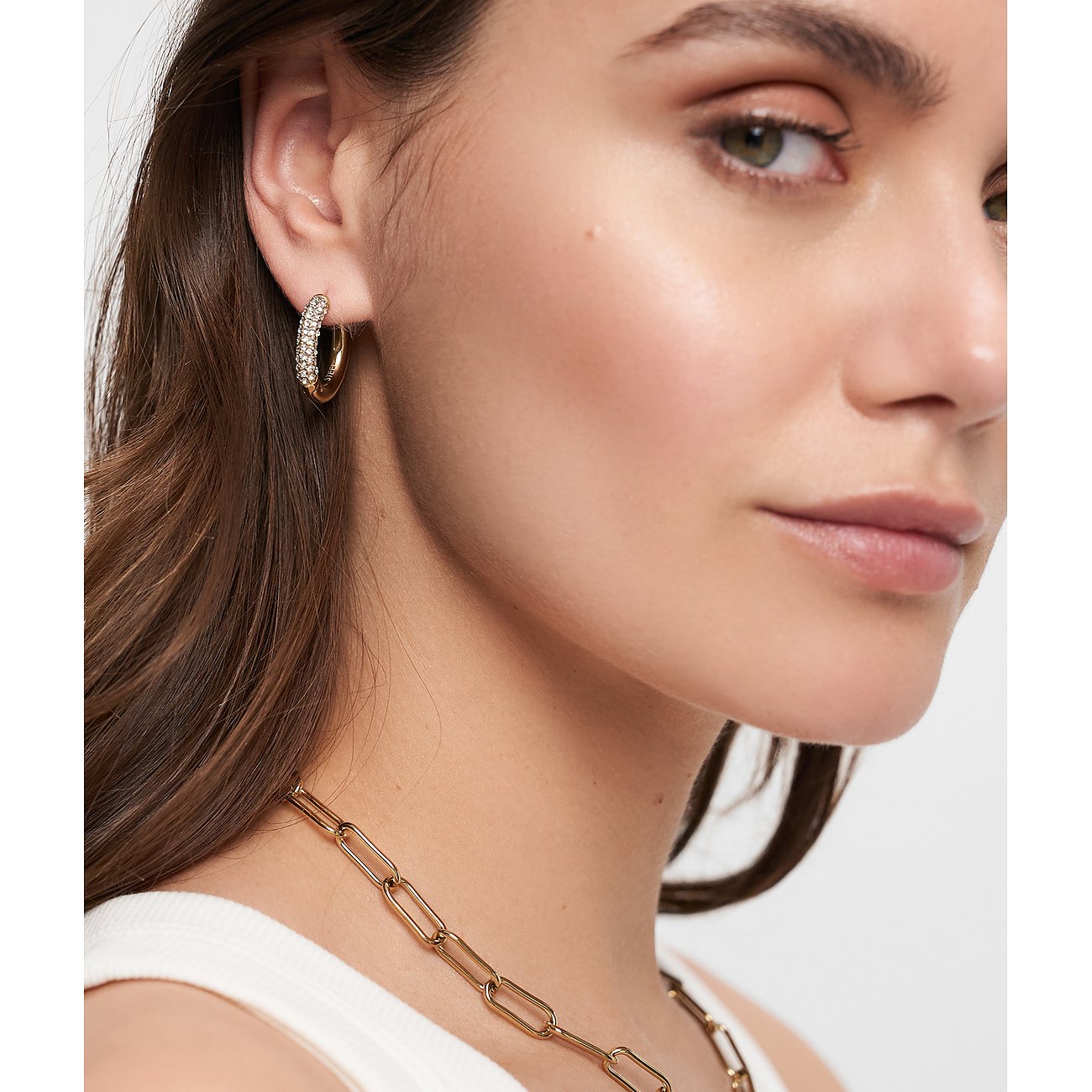 Närbild av kvinna med gyllene Tamaris creoler i rostfritt stål, besatta med gnistrande glasstenar.