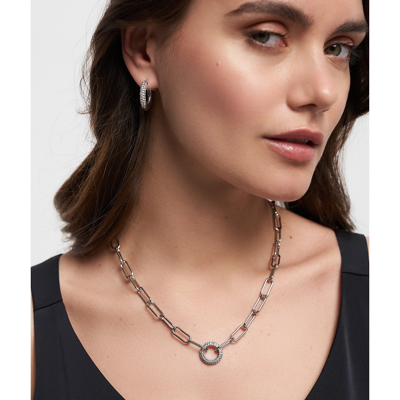 Eine Frau trägt eine Tamaris Edelstahlkette mit groben Gliedern und einem runden Anhänger mit Glassteinen.