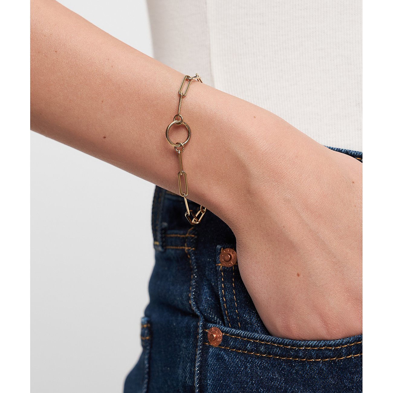Am Handgelenk getragenes Tamaris Armschmuck aus gelb-goldenem Edelstahl mit länglichen Gliedern und einem Mittelring.