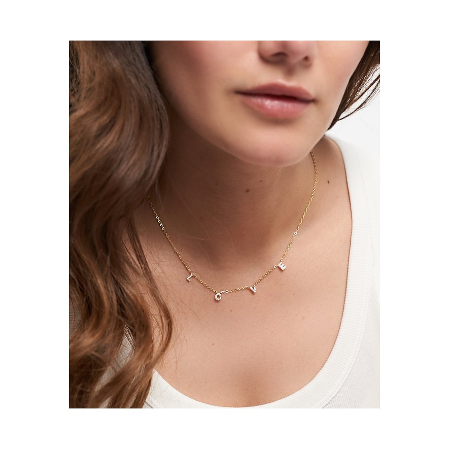 Nahaufnahme einer Frau, die eine goldfarbene Tamaris Silberkette trägt, die das Wort LOVE mit Zirkonia-Farbsteinen bildet.