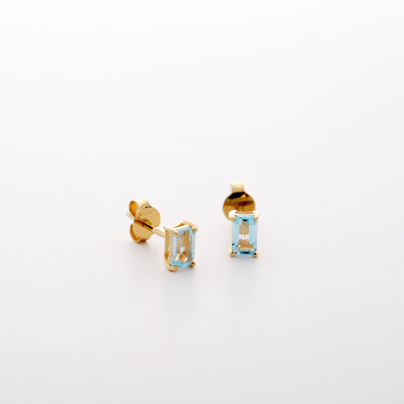 CHRIST Ohrstecker aus 585er Gelbgold mit facettierten blauen Topas im smaragdgrünen Schliff auf weißem Hintergrund.
