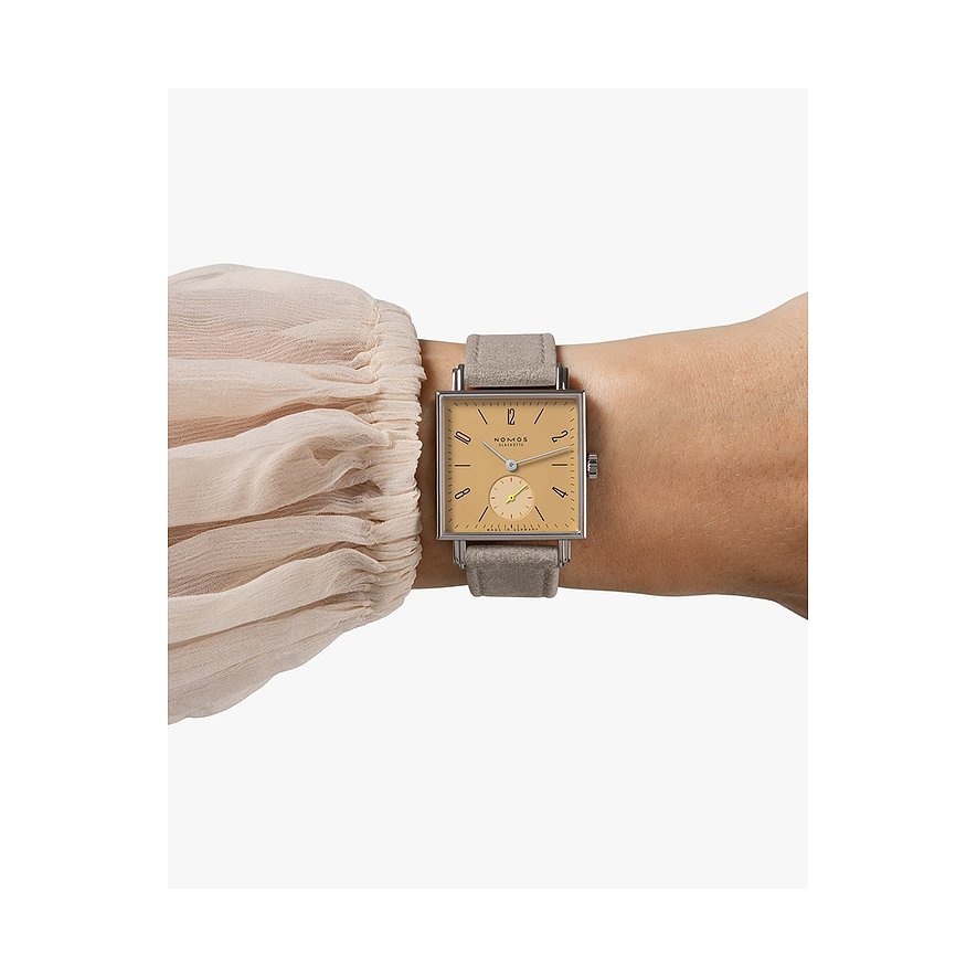 Nomos Glashütte Damenuhr aus Edelstahl mit eckigem, beigem Zifferblatt und grauem Band am Handgelenk, Nahaufnahme.