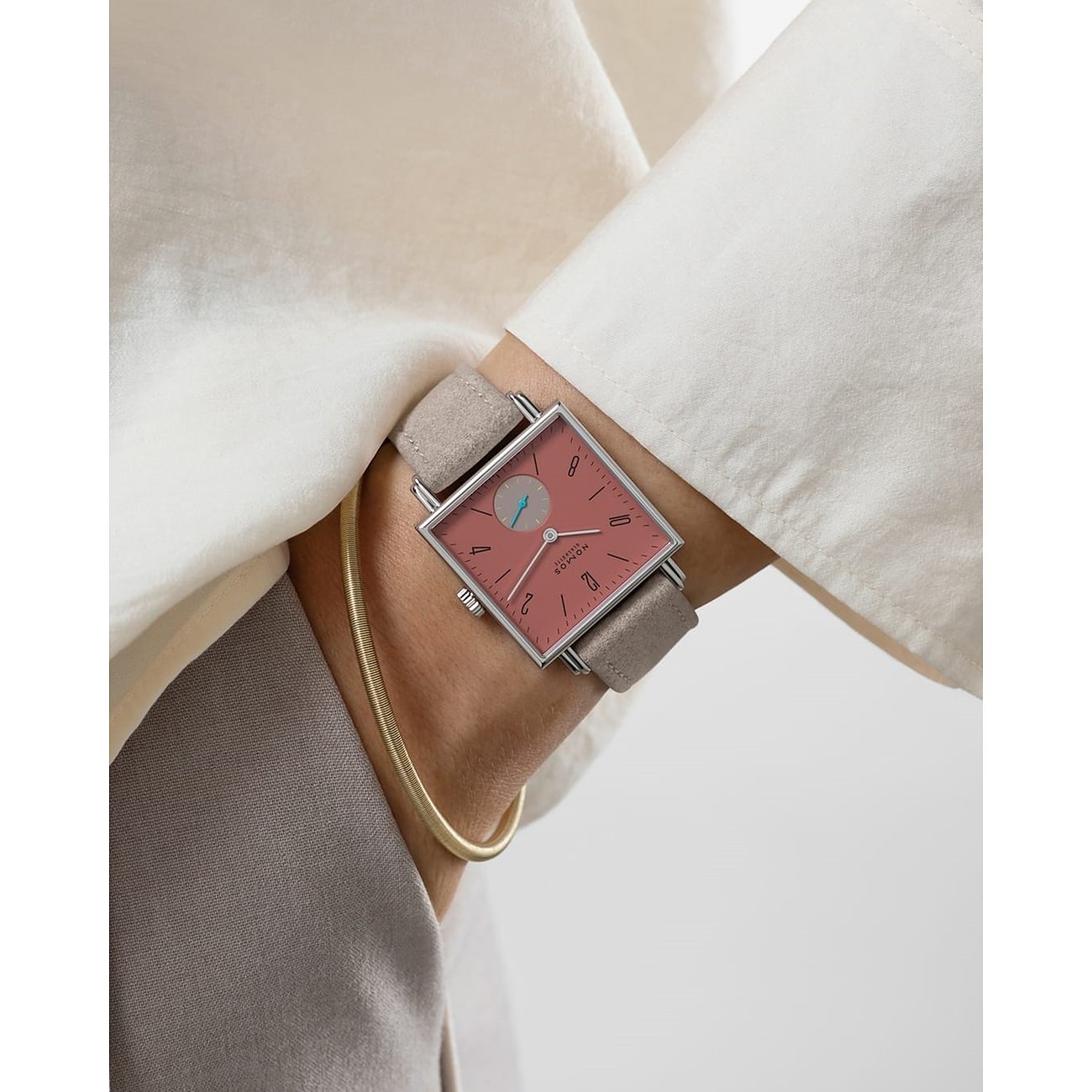 Am Handgelenk getragen, die Nomos Glashütte Damenuhr aus Edelstahl mit quadratischem rosafarbenem Zifferblatt.