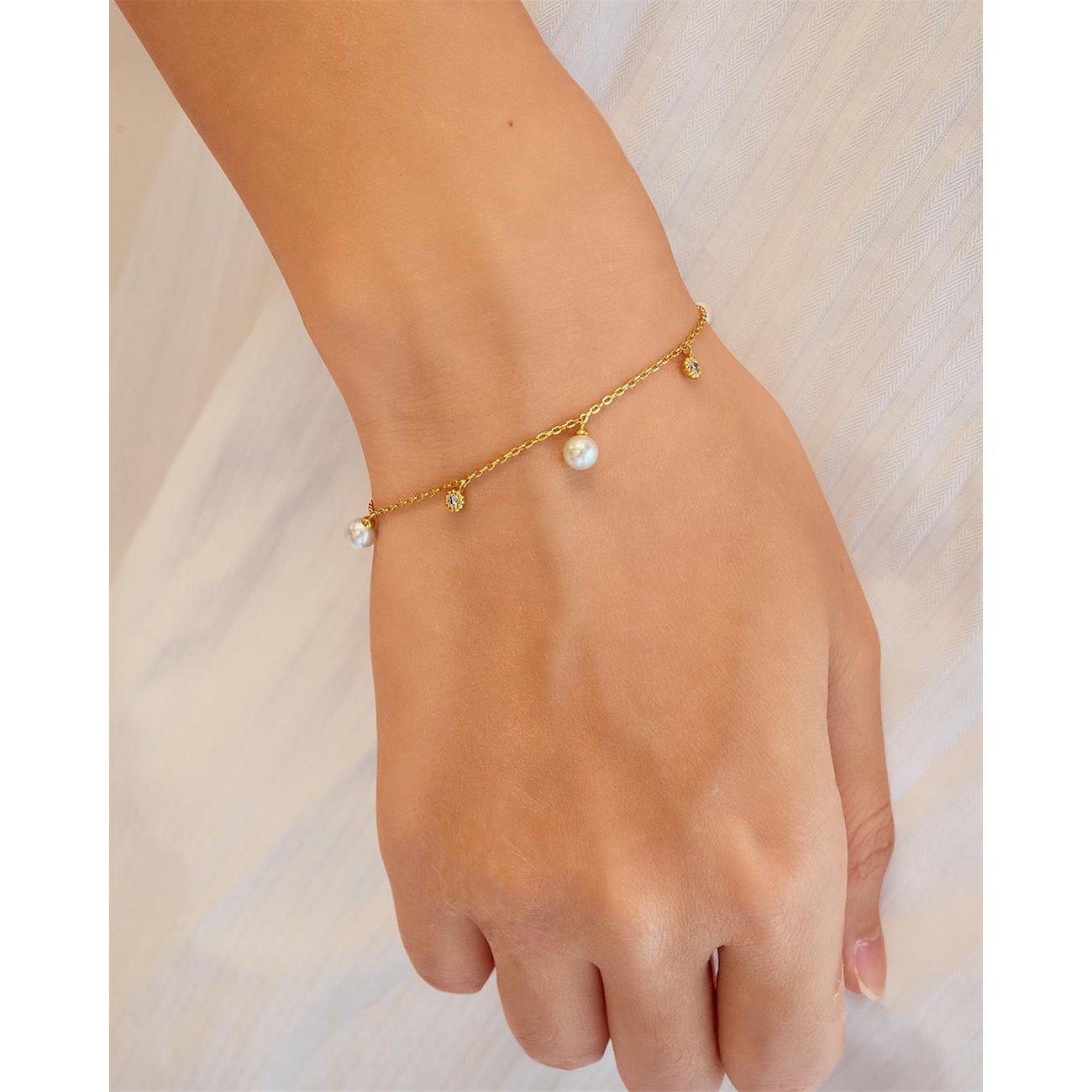 Ania Haie Armband aus vergoldetem Silber mit Zirkonia- und Perlenanhängern am Handgelenk getragen.