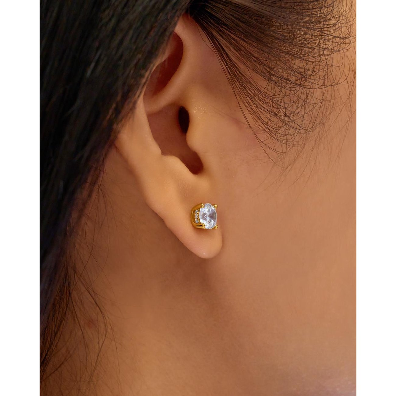 Ein Ania Haie Ohrstecker aus vergoldetem Silber mit rundem Zirkonia, getragen am Ohr eines Models.