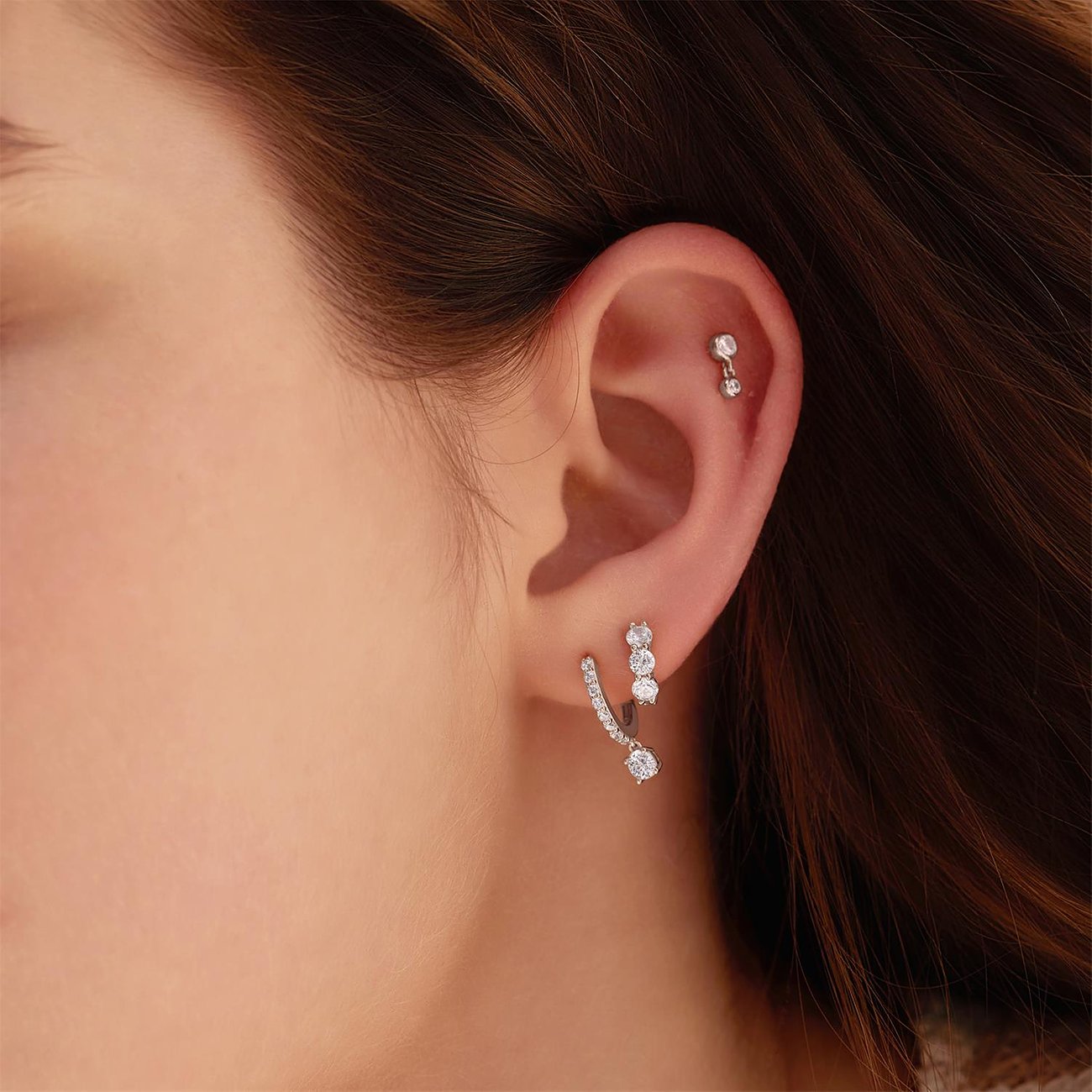 Un orecchino Ania Haie in argento con zirconi adorna l'orecchio di una modella, rivolto verso la fotocamera.