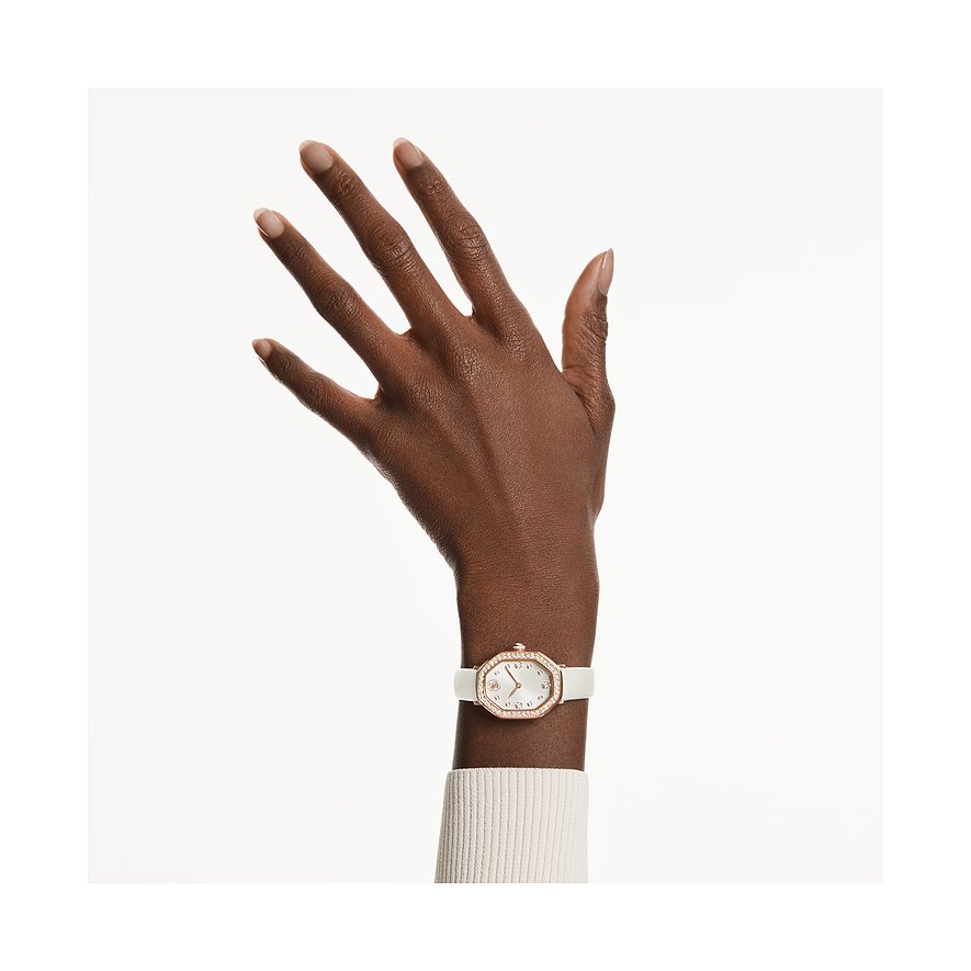 Swarovski Damenuhr mit weißem Lederarmband, roségoldenem Gehäuse und Kristallen am Handgelenk einer Person.