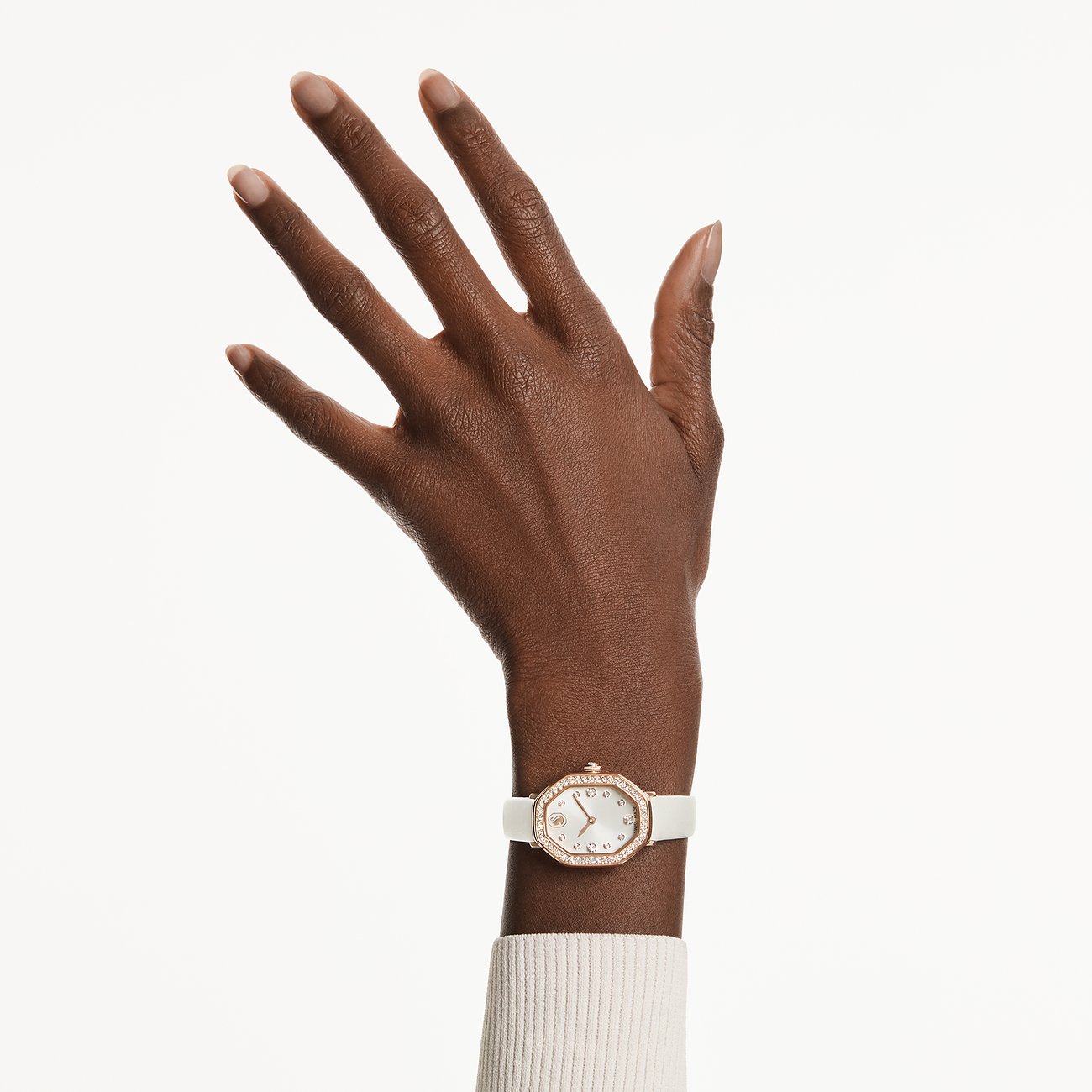 Swarovski Damenuhr mit weißem Lederarmband, roségoldenem Gehäuse und Kristallen am Handgelenk einer Person.