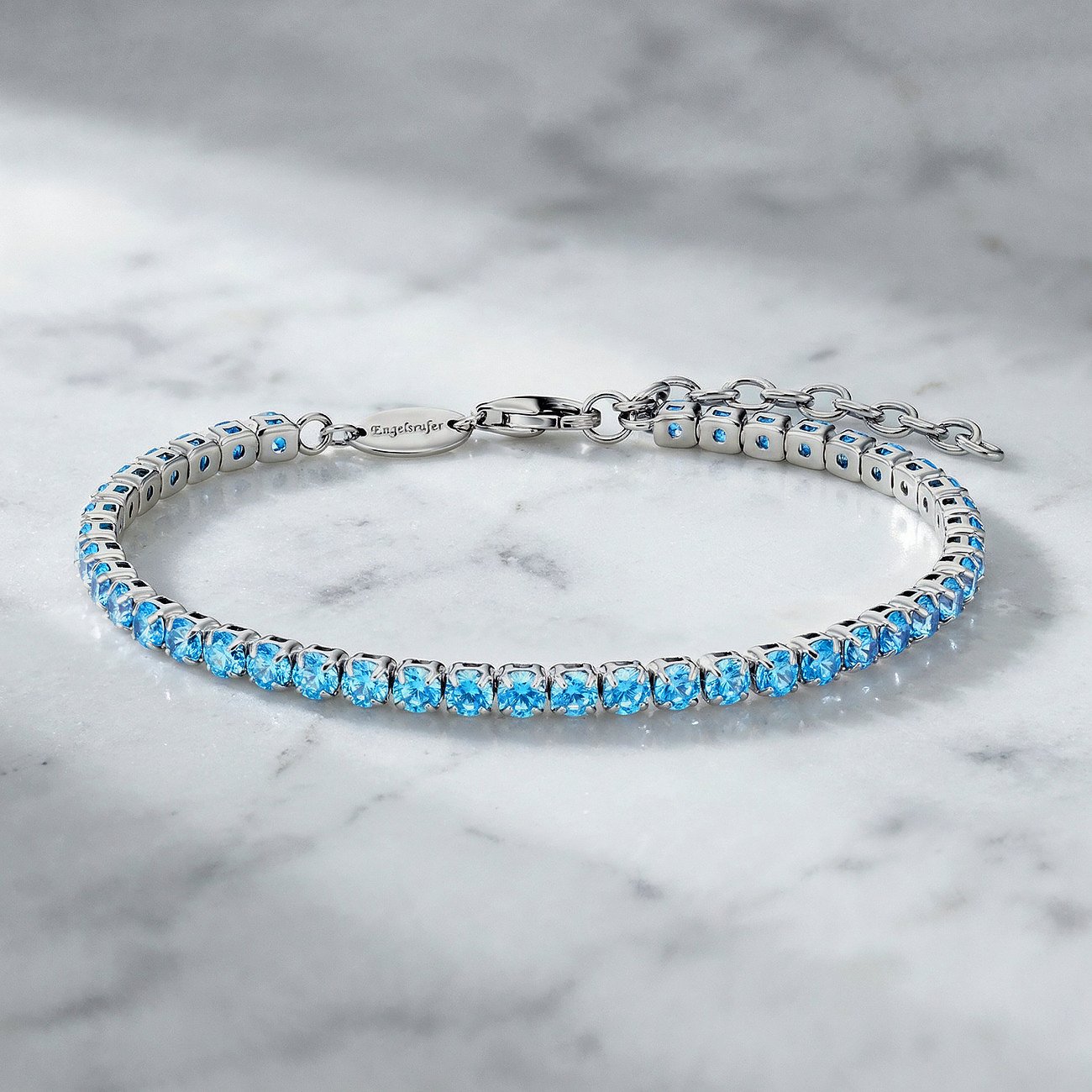 Engelsrufer Armband aus 925er Silber mit einer Reihe blauem Zirkonia, liegend auf einer weißen Marmoroberfläche.