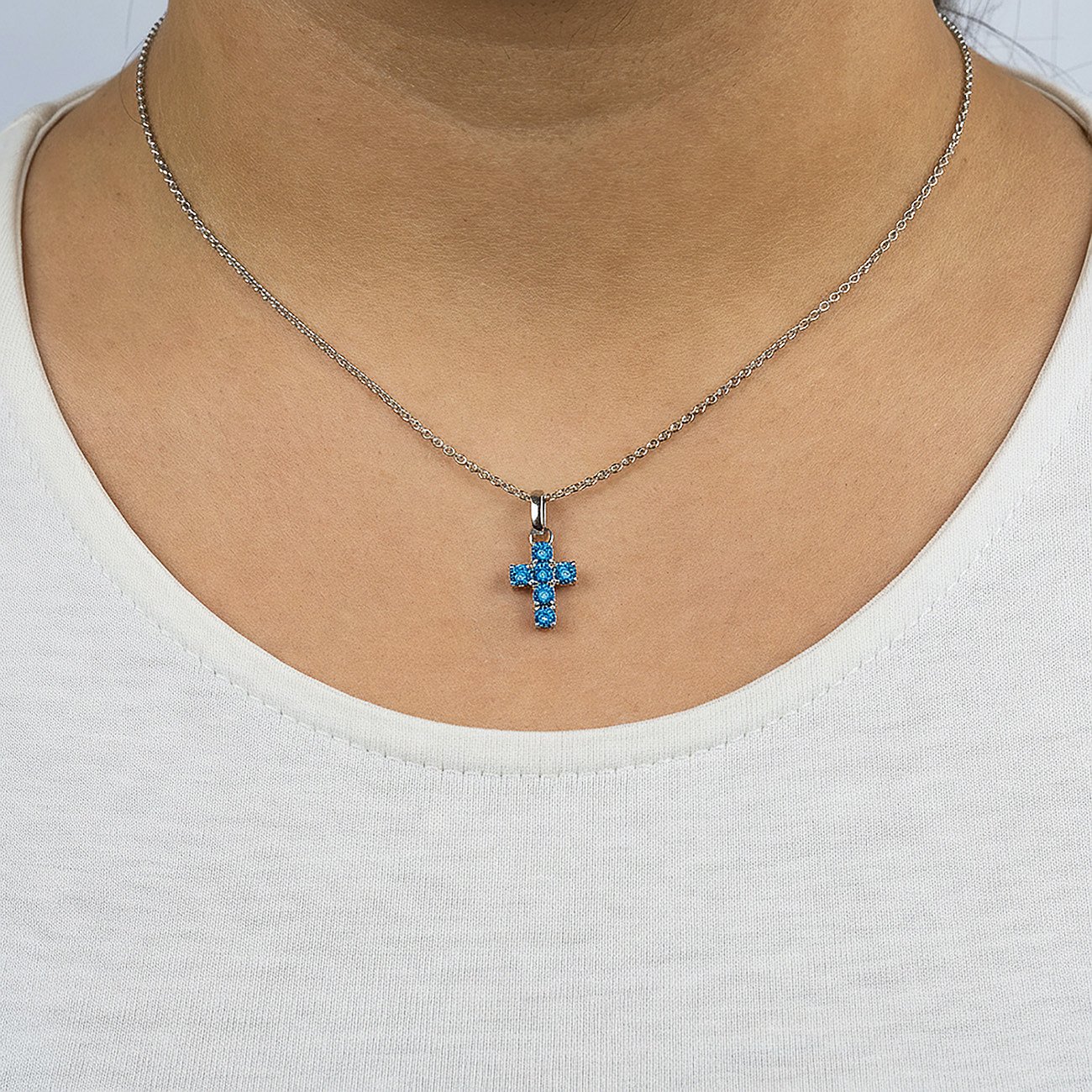 Engelsrufer Halsschmuck: Silberne Kette mit einem Kreuzanhänger, besetzt mit blauen Zirkonia Farbsteinen, getragen.