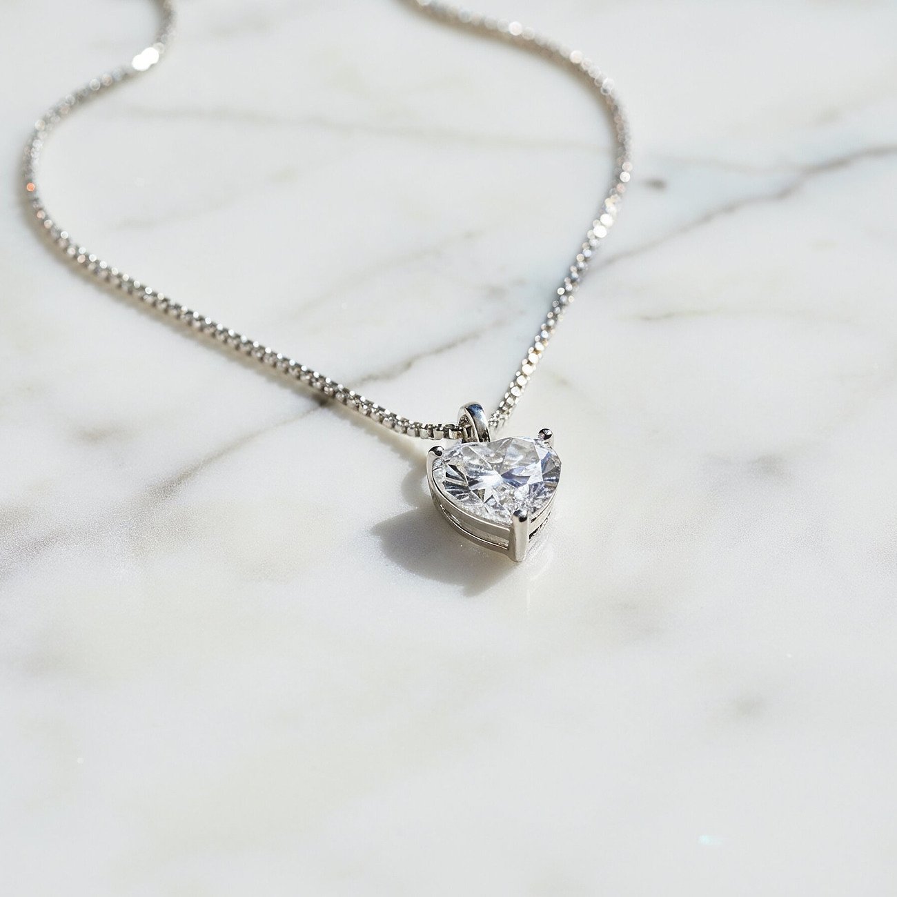 Engelsrufer Halskette aus 925er Silber mit herzförmigem Zirkonia-Anhänger, auf weißem Marmor liegend.
