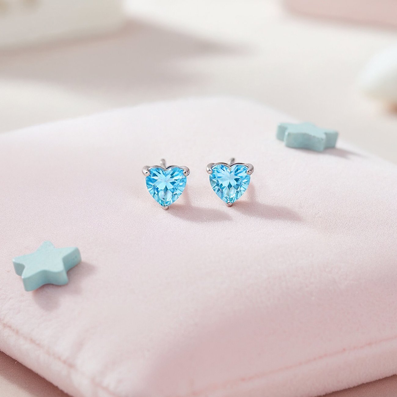 Engelsrufer roestvrijstalen oorknopjes met hartvormige lichtblauwe zirkonia kleurstenen op een roze ondergrond.