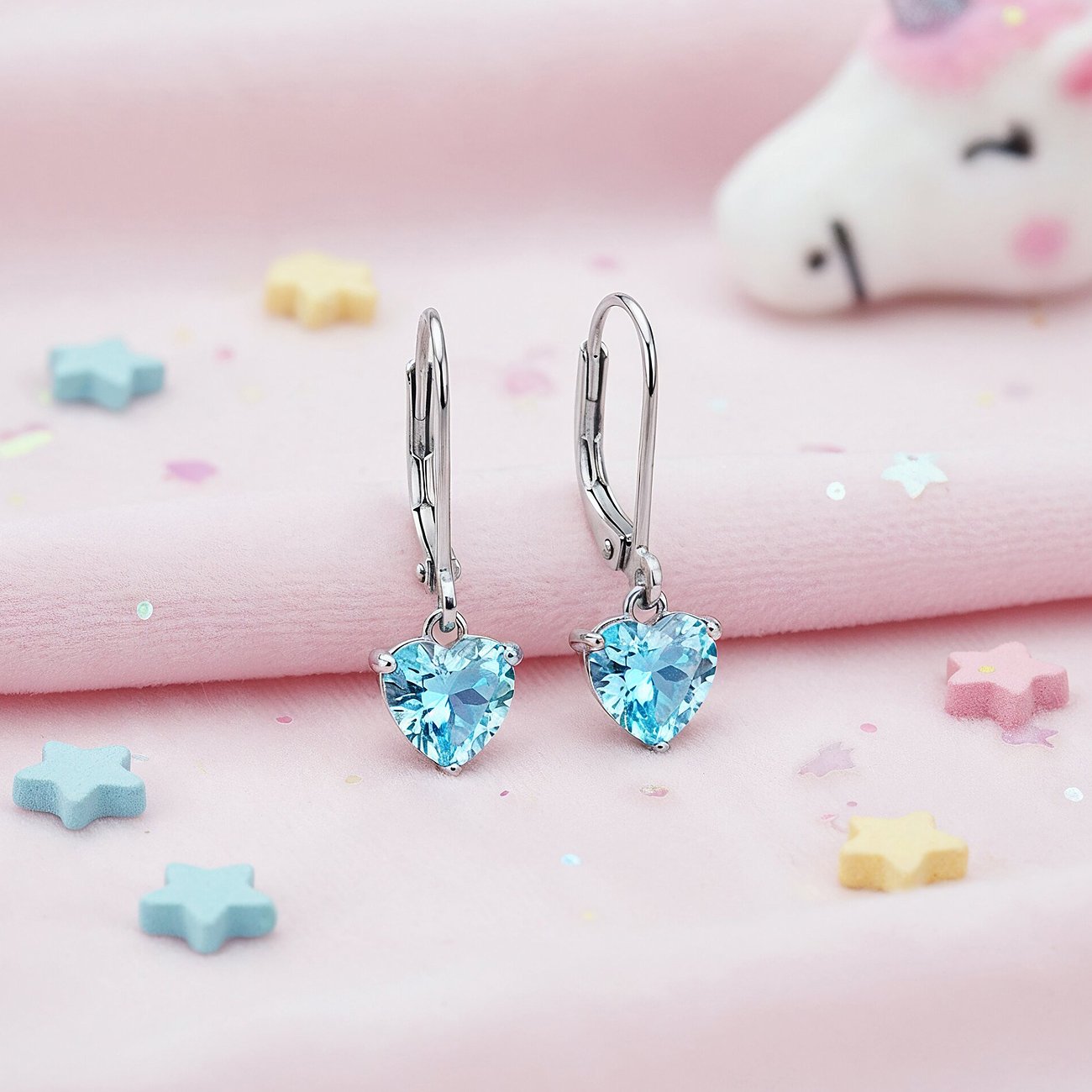 Engelsrufer Ohrschmuck aus Edelstahl mit herzförmigen blauen Zirkonia-Farbsteinen auf rosafarbenem Untergrund.