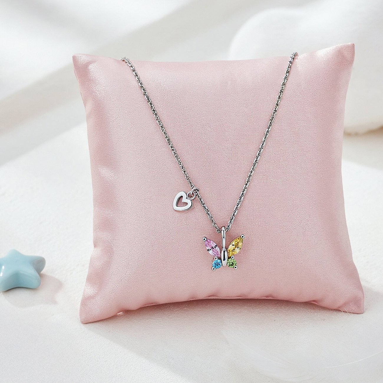 Engelsrufer Edelstahl-Halskette mit buntem Zirkonia-Schmetterlingsanhänger, auf rosa Kissen liegend.