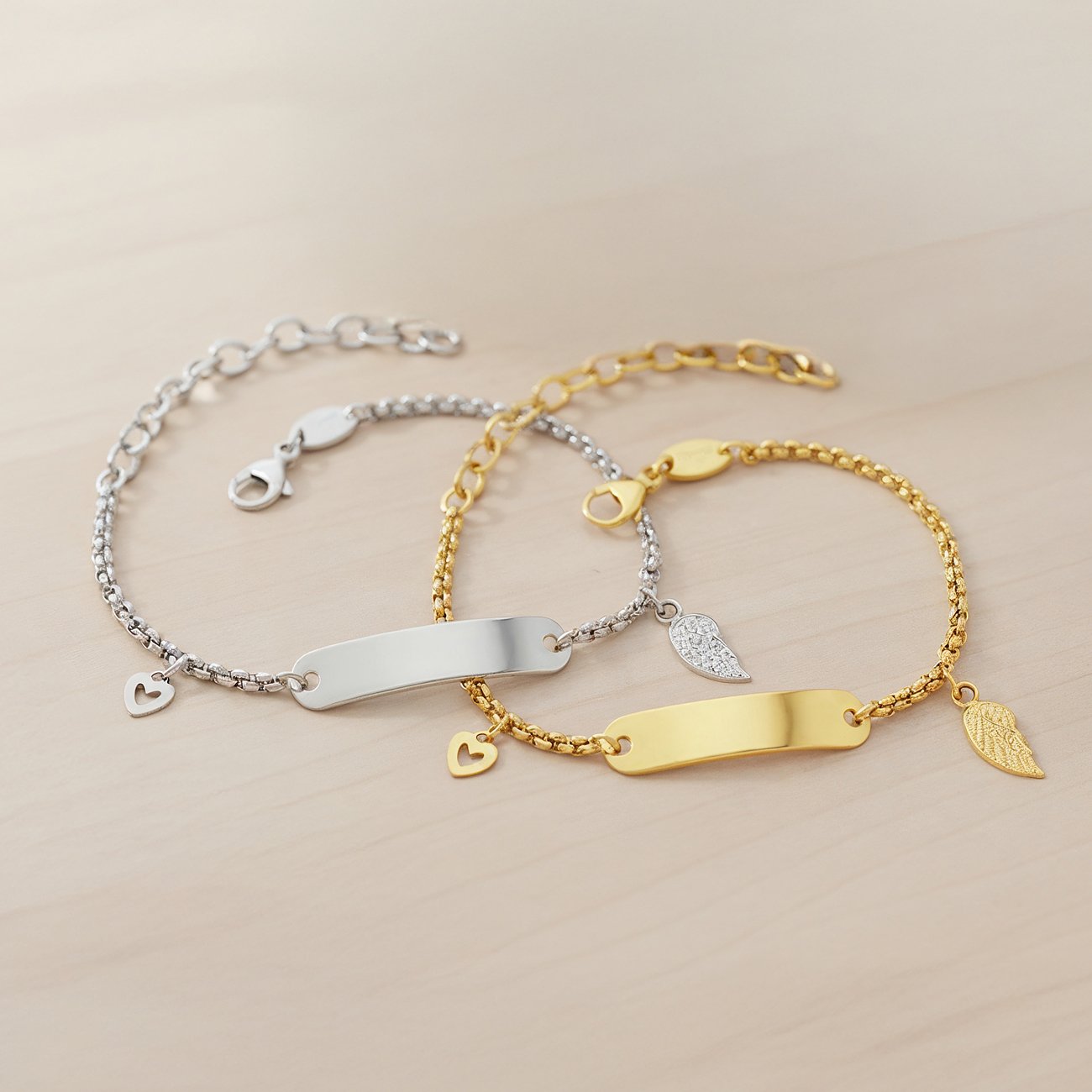 Zwei Engelsrufer Edelstahl-Armbänder (silber/gold) mit Plakette und Engelsflügel-Anhängern im Vordergrund.