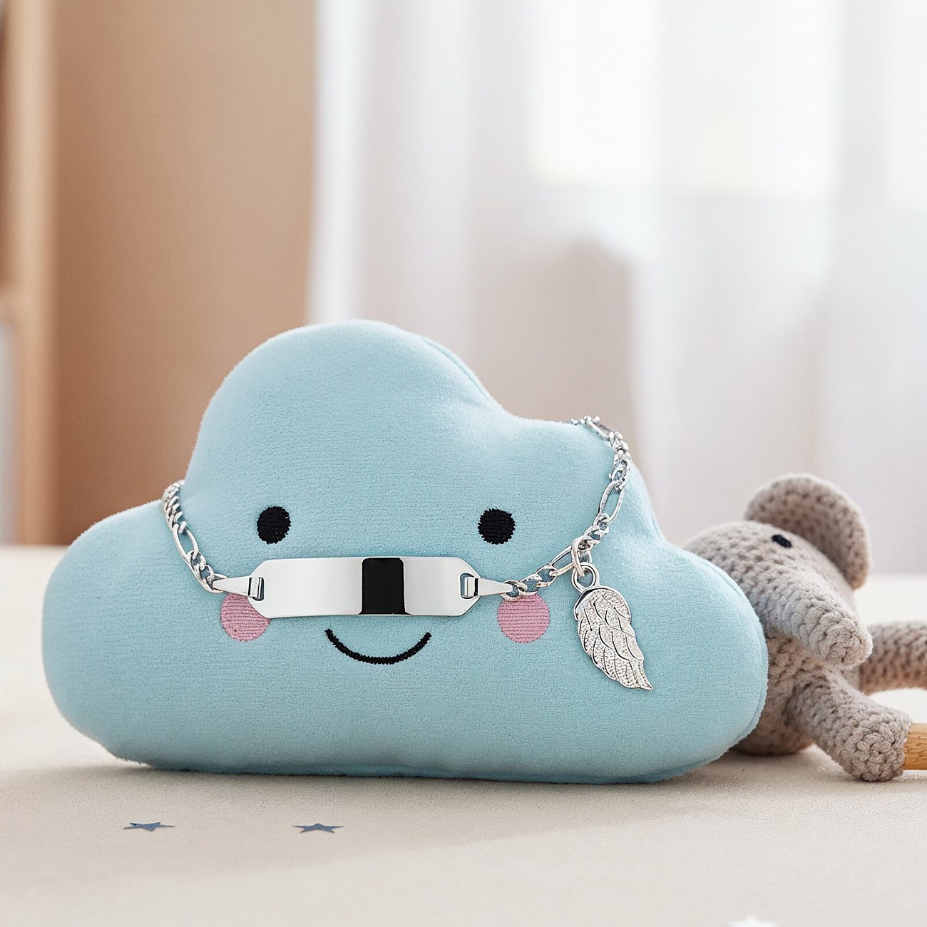 Engelsrufer Armschmuck aus Edelstahl, ein Armband mit Gravurplatte und Flügelanhänger, auf Wolkenkissen liegend.