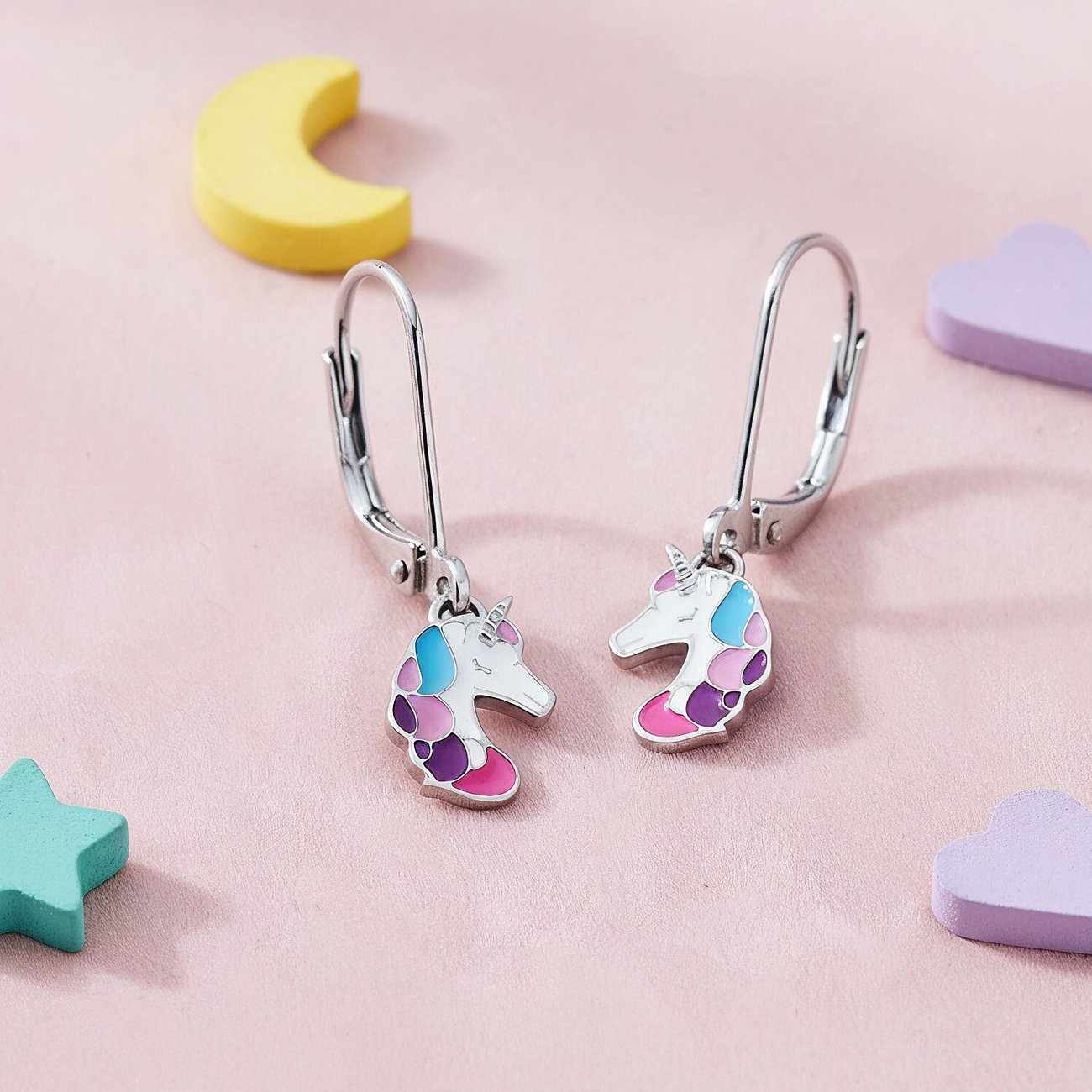 Engelsrufer enhörningsörhängen i rostfritt stål och emalj, visade mot en rosa bakgrund.