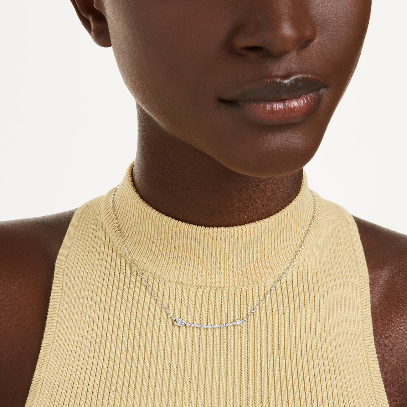 Nahaufnahme eines silberfarbenen Swarovski Halschmuckes mit Pfeilmotiv und Kristallen auf dem Dekolleté eines Models.