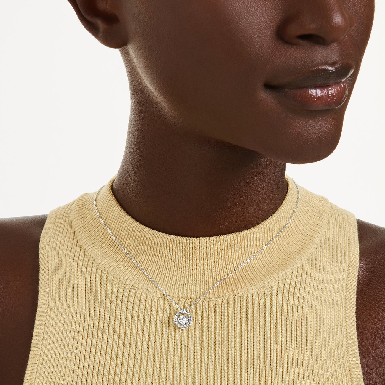 Ein Swarovski Halsschmuck aus Metall mit Swarovski-Kristall hängt um den Hals eines Models, das ein gelbes Oberteil trägt.