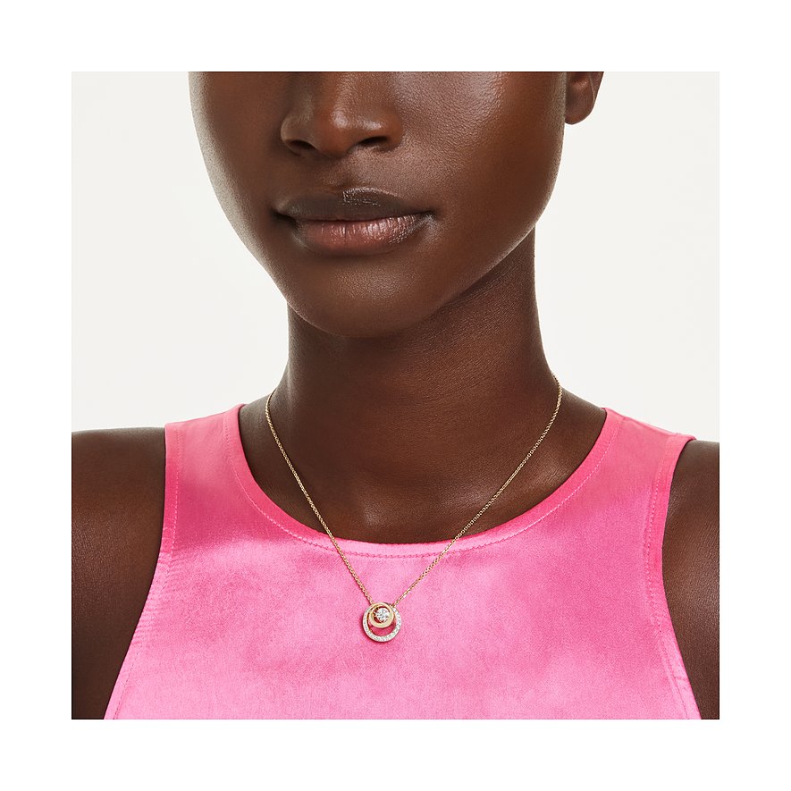 Eine Frau trägt eine goldene Swarovski Metall-Halskette mit einem runden Anhänger aus funkelnden Farbkristallen.