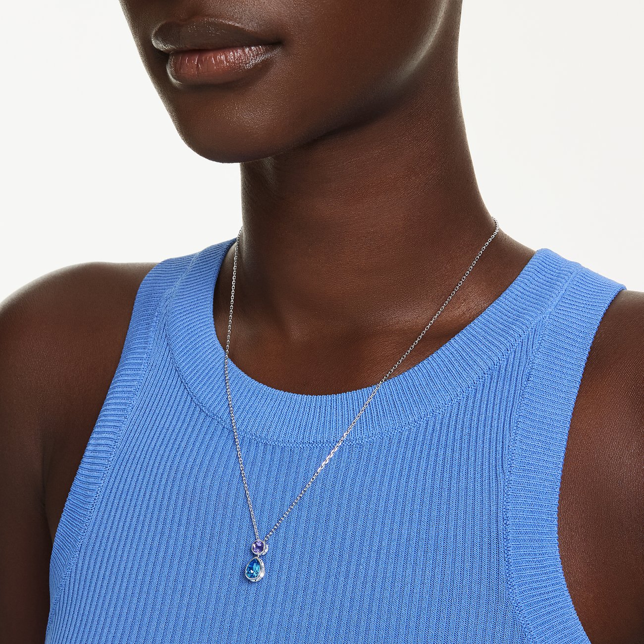 Nahaufnahme einer Person, die eine Swarovski Metall-Halskette mit zwei runden bunten Swarovski-Kristallanhängern trägt.